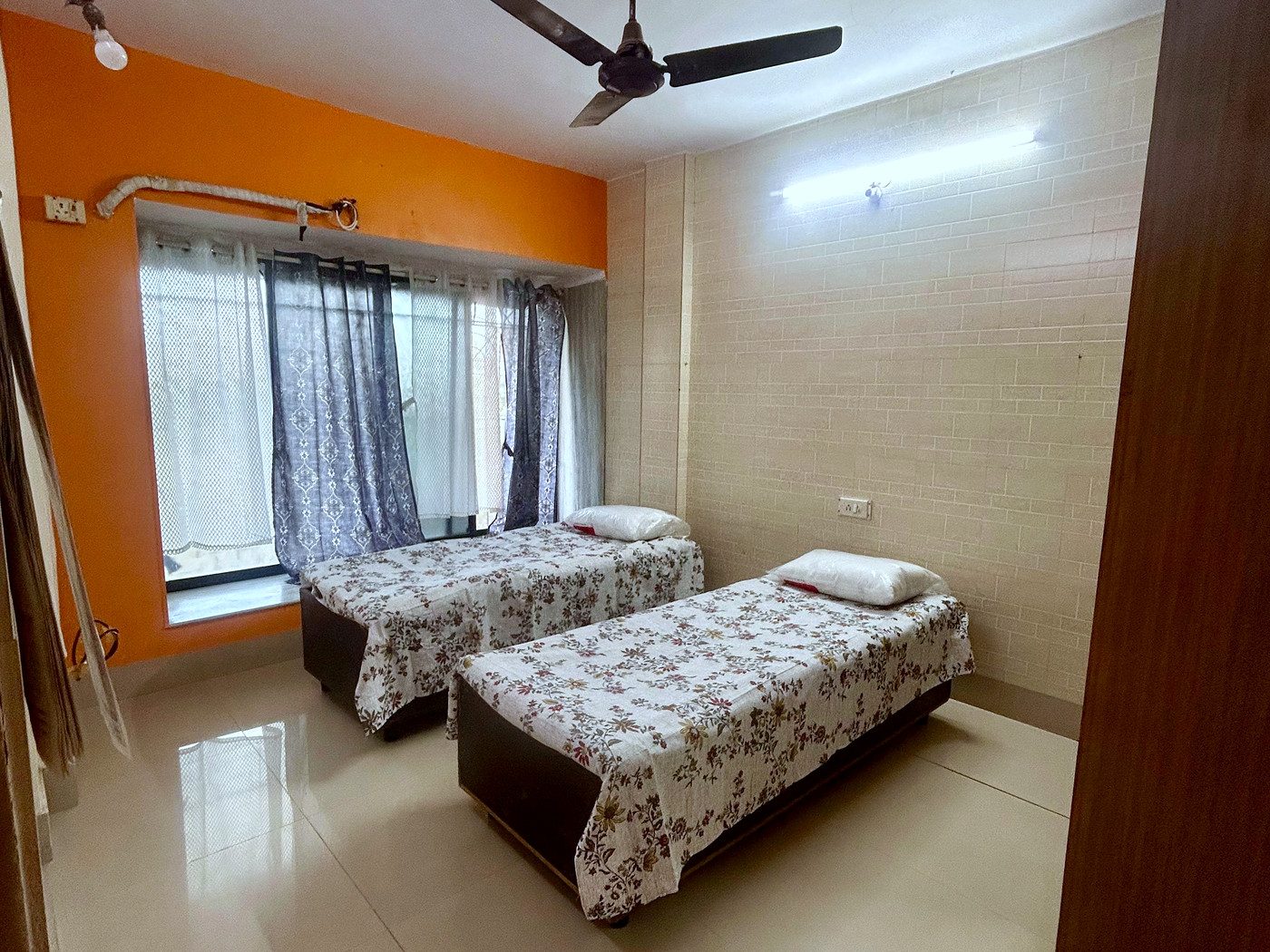 A sharing room with beds set apart, a curtained window and a warm accent wall